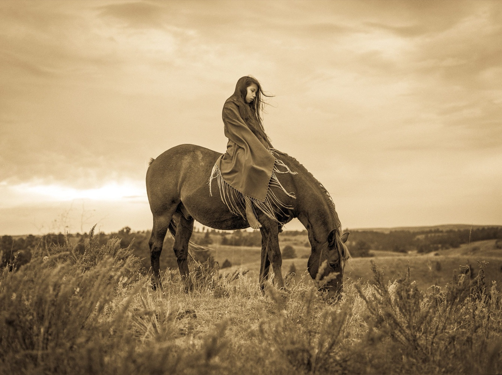 A child riding bareback as the horse grazes on the prairie