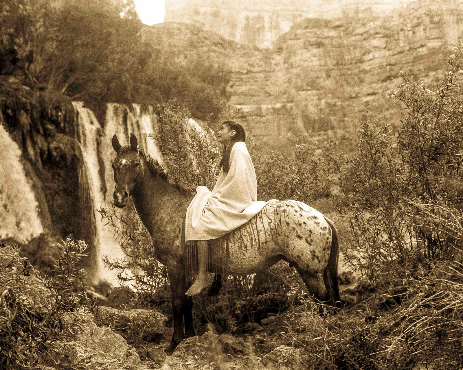 A woman on an Appaloosa beside a cliff waterfall