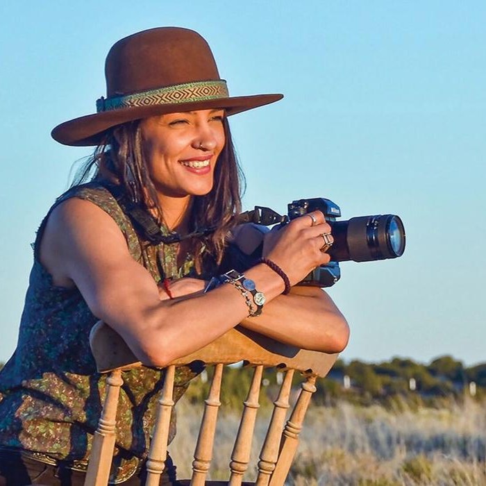 Portrait of photographer Zoë Marieh Urness in a wide-brim hat, holding her camera at golden hour